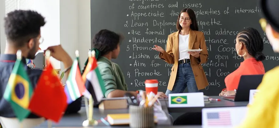 Docente impartiendo una clase bilingüe ante una pizarra escrita en inglés